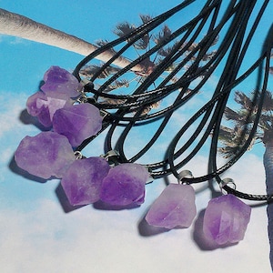 May include: A set of ten amethyst crystal necklaces with black cords. Each necklace features a raw, purple amethyst crystal pendant.