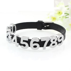 May include: A black silicone bracelet with silver metal number charms. The numbers on the bracelet are 3, 4, 5, 6, 7, 8, and 9.