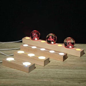 Może przedstawiać: Drewniane podstawy świetlne z wbudowanymi światłami LED i przezroczystymi szklanymi kulami. Kule mają czerwone akcenty i spoczywają na drewnianych podstawach. Podstawy są połączone białymi przewodami. Ogólnym tematem jest oświetlenie dekoracyjne.