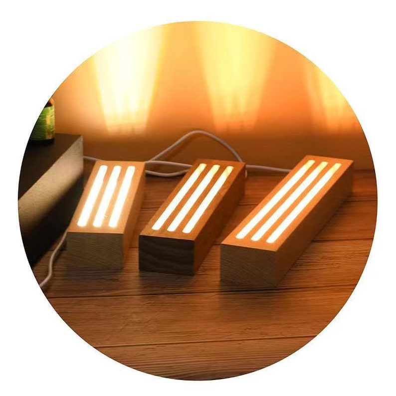 Puede incluir: Tres l&aacute;mparas rectangulares de madera con una luz blanca c&aacute;lida que emana de la parte superior. Las l&aacute;mparas est&aacute;n dispuestas en fila sobre una superficie de madera.