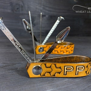 Könnte beinhalten: Ein Multifunktions-Pfeifenwerkzeug mit einer Ledertasche. Das Werkzeug verfügt über einen Stopfer, einen Poker und ein Reinigungswerkzeug. Die Tasche ist aus braunem Leder mit einem gewebten Muster und den eingeprägten Initialen "PP".