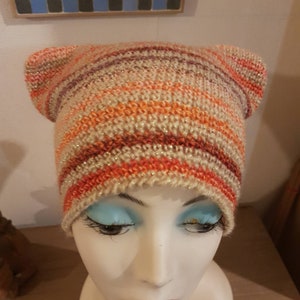 Peut inclure: Un bonnet en tricot rayé avec des oreilles en orange, marron et beige. Le bonnet a une finition scintillante.