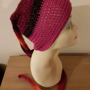 Peut inclure: Un bonnet crocheté à la main dans les tons de rose, noir et orange. Le chapeau a une longue extension en forme de queue qui passe de l'orange au rose. Le chapeau est présenté sur une tête de mannequin.