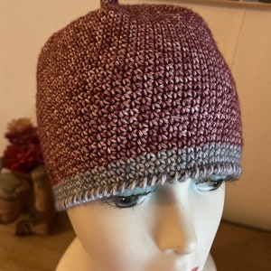 Peut inclure: Un bonnet en crochet bicolore. Le bonnet est principalement de couleur bordeaux foncé avec une bande grise plus claire en bas.