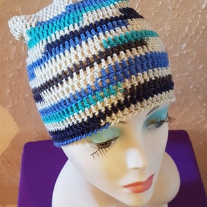 Peut inclure: Un bonnet crocheté avec un motif rayé dans les tons de bleu, blanc et gris. Le bonnet est réalisé avec un point texturé et a une coupe ample.