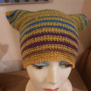 Peut inclure: Un chapeau crocheté avec des oreilles en jaune, violet et bleu. Le chapeau a une texture scintillante.