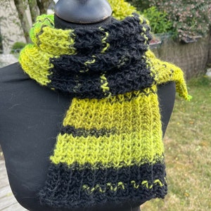 Peut inclure: Une écharpe tricotée noire et vert lime avec un motif rayé. L'écharpe est pliée et drapée sur un mannequin noir.