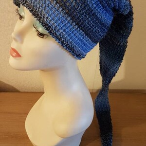 Peut inclure: Un chapeau crocheté bleu et noir avec une longue queue. Le chapeau est réalisé avec un point texturé et présente un dégradé de couleur du bleu foncé au bleu clair.