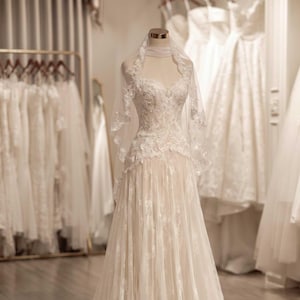 May include: A floor-length ivory wedding dress featuring a sweetheart neckline, intricate lace bodice, and a flowing tulle skirt with lace appliques. The gown is paired with a matching sheer lace-trimmed veil draped over the shoulders.
