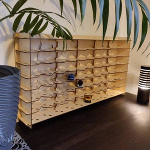 May include: A wooden display shelf with multiple slots for storing small items, such as toy cars. The shelf is made of light brown wood and has a natural finish. There are several toy cars in the slots, including a blue car, a red car, and a black car.