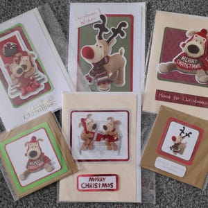May include: A set of six Christmas cards featuring a variety of designs with a festive theme. The cards feature illustrations of reindeer, penguins, and other holiday characters. The cards are decorated with red, green, and gold accents. The text on the cards reads "Christmas Wishes", "Home for Christmas", and "Merry Christmas".