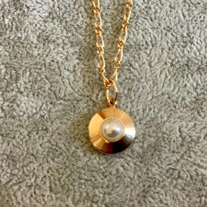 May include: A gold chain necklace with a round pendant featuring a white pearl in the center.