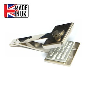 May include: A silver metal stamp with a handle and a square base. The base has a small knob on top and the text "MADE IN UK" is printed on the base.