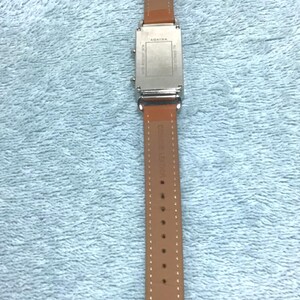 May include: A rectangular silver watch with a brown leather band. The watch face is silver, and the band is a light brown color. The watch is labeled "AGATHA" on the band and the back of the watch.