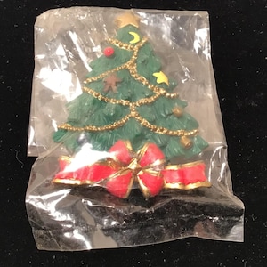 May include: A green Christmas tree ornament with a red bow, gold trim, and various decorations. The ornament is packaged in a clear plastic bag.