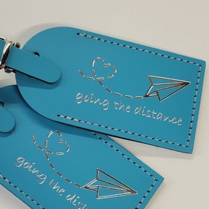 May include: Two blue luggage tags with silver lettering that reads "going the distance" and a paper airplane graphic.