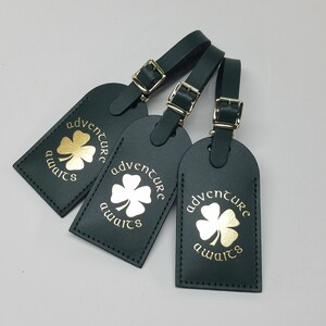 May include: Three dark green leather luggage tags with gold clover designs and the text "adventure awaits".