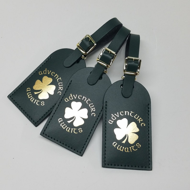 May include: Three dark green leather luggage tags with gold clover designs and the text "adventure awaits".