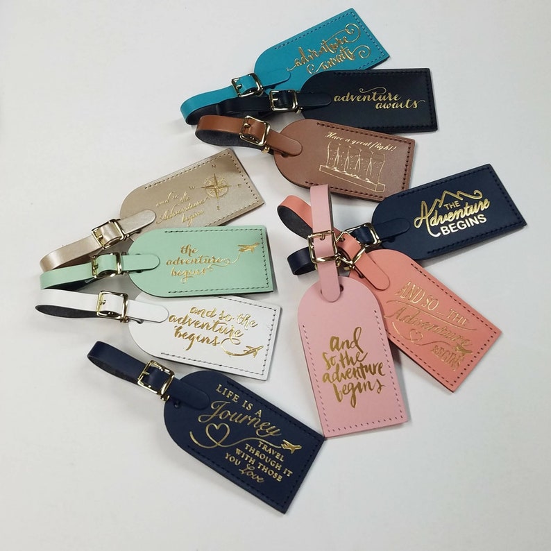 May include: Ten leather luggage tags with gold lettering. The tags feature various travel-themed quotes, including "Life is a Journey", "And so the adventure begins", and "The adventure begins".