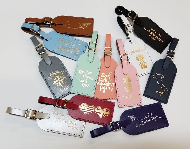 May include: A collection of ten leather luggage tags with gold lettering. The tags feature various travel-themed designs and phrases, including "Let the Adventure Begin", "Oh, the Places You'll Go!" and "And So the Adventure Begins".