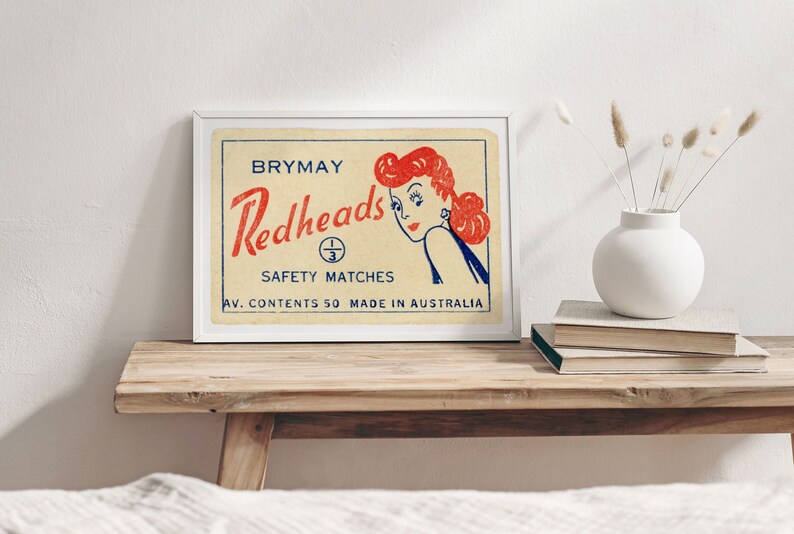 May include: A vintage framed print of a matchbox label for Brymay Redheads Safety Matches. The label features a cartoon illustration of a woman with red hair looking over her shoulder. The text on the label reads "Brymay Redheads Safety Matches Av. Contents 50 Made in Australia."