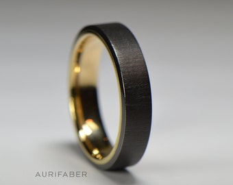 May include: A black and gold wedding band with a brushed finish. The band has a thin gold band around the edge.