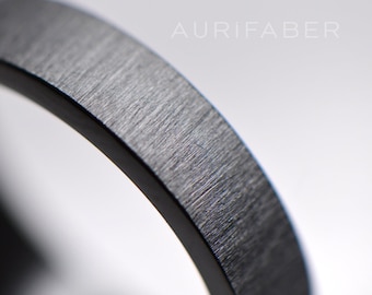 May include: Close-up of a brushed silver ring band. The surface of the band has a fine, textured finish.