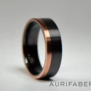 May include: A black and rose gold wedding band with a brushed finish. The band has a thin rose gold inlay around the edge.