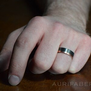 May include: A black and rose gold wedding band with a beveled edge.