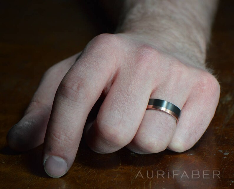 May include: A black and rose gold wedding band with a beveled edge.