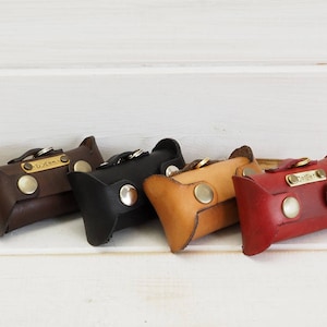 Könnte beinhalten: Fünf Leder-Schlüsselanhänger in verschiedenen Farben, jeder mit einem personalisierten Metalletikett. Die Schlüsselanhänger sind braun, schwarz, beige und rot.