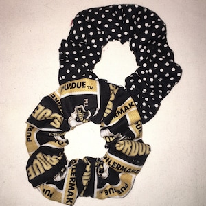 May include: A black and white scrunchie with two distinct fabric patterns. One side features white polka dots on a black background, while the other displays the Purdue Boilermakers logo in black and gold.