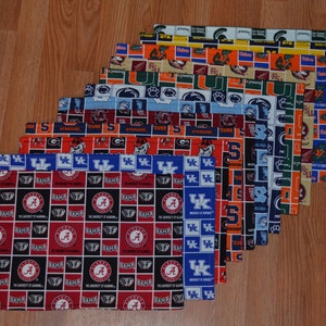 Puede incluir: Una colección de manteles individuales rectangulares de tela con logotipos y colores de varios equipos universitarios. Los manteles individuales muestran logotipos de equipos como Alabama, Syracuse y Kentucky. Los colores dominantes son el rojo, el azul y el naranja.