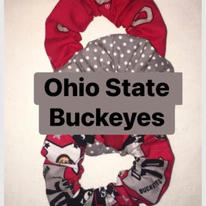 Könnte beinhalten: Drei Stoff-Haargummis in Rot, Grau und Weiß. Ein rotes Haargummi hat ein weißes "O"-Logo, ein anderes ist grau mit weißen Punkten, und das dritte hat ein rot-graues Muster mit dem Text "Buckeyes". Der Text "Ohio State Buckeyes" befindet sich in der Mitte.