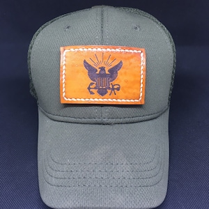 May include: A green mesh baseball cap with a brown leather patch featuring a black eagle and anchor design.