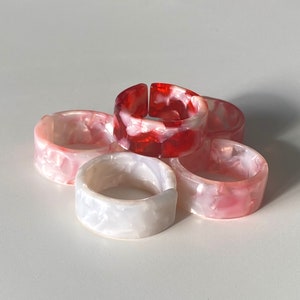 May include: Five resin rings in a variety of colors and patterns. The rings are stacked on top of each other. The rings are made of a translucent material and have a marbled effect.