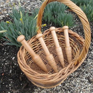 May include: Four wooden plant stakes in a wicker basket. The stakes are brown and have a pointed end. The basket is brown and has a woven design.
