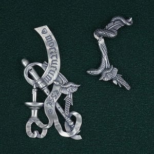 May include: Two silver-toned pendants, one with a snake wrapped around a feather and the other with a scroll inscribed with the words "Memento Mori" and a skull, a bird, and a pipe.