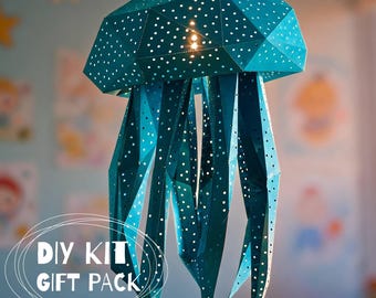 May include: A teal geometric jellyfish-shaped hanging lamp made of folded paper with numerous small circular cutouts that allow light to shine through. The text DIY KIT GIFT PACK is printed in white at the bottom left of the image.