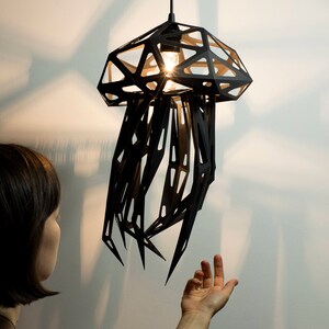 May include: A black metal pendant light shaped like a jellyfish with a geometric design. The light is hanging from the ceiling and is illuminated by a light bulb.