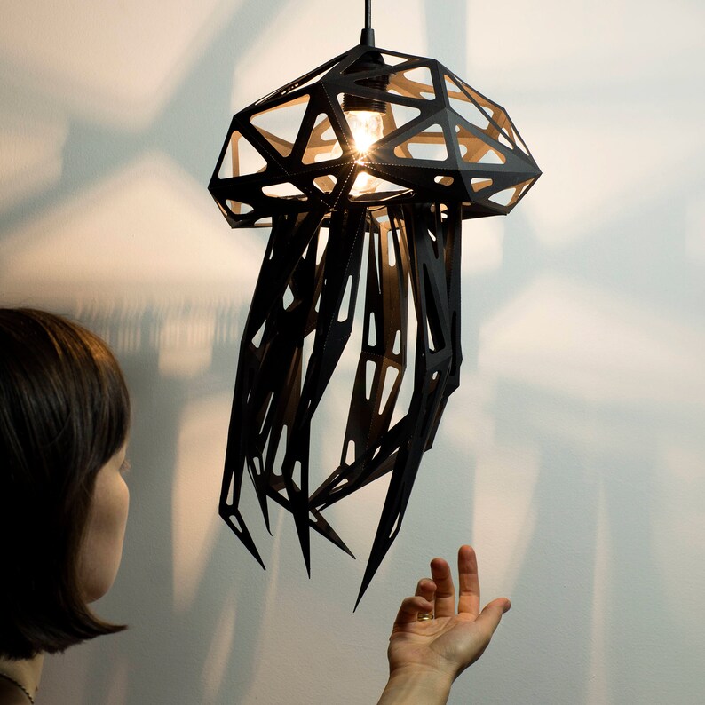May include: A black metal pendant light shaped like a jellyfish with a geometric design. The light is hanging from the ceiling and is illuminated by a light bulb.