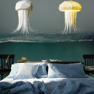 K&ouml;nnte beinhalten: Zwei wei&szlig;e Papier-Medusen-Pendelleuchten h&auml;ngen &uuml;ber einem blauen Bett mit wei&szlig;en Kissen. Der Hintergrund ist ein Wandbild mit einer Ozeanszene.