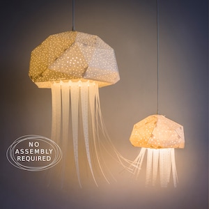 Può includere: Due lampade a sospensione a forma di medusa in carta bianca con un motivo a pois e frange bianche. Le lampade sono appese al soffitto e sono illuminate. Il testo "NO ASSEMBLY REQUIRED" è visibile nell'immagine.