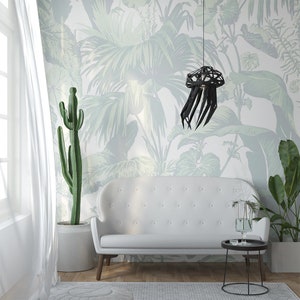 May include: A white sofa with a black, geometric, jellyfish-shaped pendant light hanging above it. The wall behind the sofa is covered in a green and white tropical leaf wallpaper.