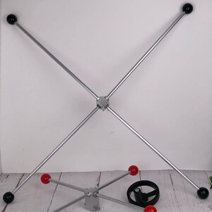 May include: Two silver metal structures with black and red spheres. One structure is a cross shape with black spheres at the ends. The other is a star shape with red spheres. A black wheel is also present.