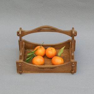 Peut inclure: Un panier en bois avec une poignée, rempli de quatre mandarines orange vif. Le panier est en bois brun clair et de forme rectangulaire. Des feuilles vertes sont attachées à certaines mandarines.