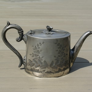 以下が含まれることがあります： 曲線的なハンドルと注ぎ口が付いた銀色のティーポット。ティーポットは、本体と蓋に花の彫刻が施された装飾的なデザインが特徴です。ハンドルと注ぎ口には装飾的なディテールが施されています。