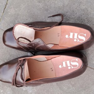 May include: A pair of brown leather dress shoes with laces. The insoles are light brown with the word "Sir" printed in white. The shoes are size 43.