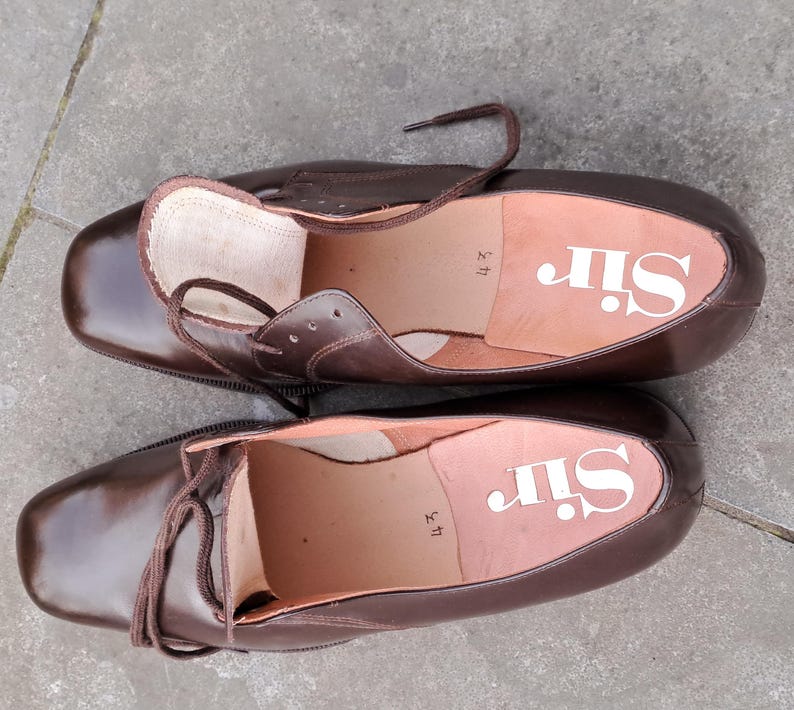 May include: A pair of brown leather dress shoes with laces. The insoles are light brown with the word "Sir" printed in white. The shoes are size 43.