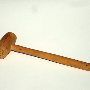 May include: A wooden meat mallet with a textured, square-patterned head and a long, smooth handle. The mallet is made of light-colored wood and is designed for tenderizing meat.